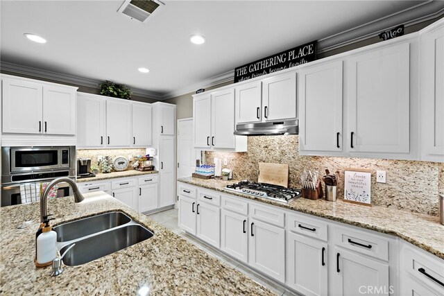 kitchen featuring stainless steel appliances, under cabinet range hood, a sink, tasteful backsplash, and white cabinets