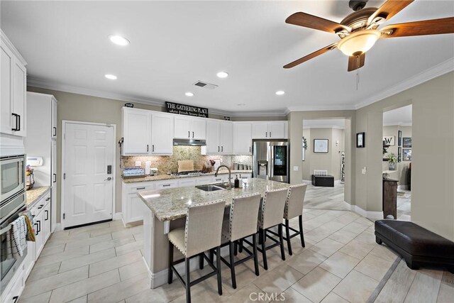 kitchen with appliances with stainless steel finishes, a sink, under cabinet range hood, decorative backsplash, and a kitchen bar