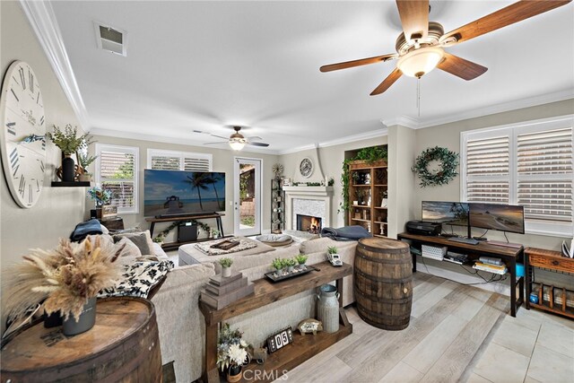 living room with ceiling fan, a warm lit fireplace, crown molding, and wood finished floors