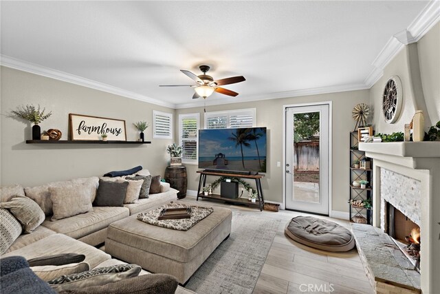 living room with crown molding, ceiling fan, wood finished floors, a warm lit fireplace, and healthy amount of natural light