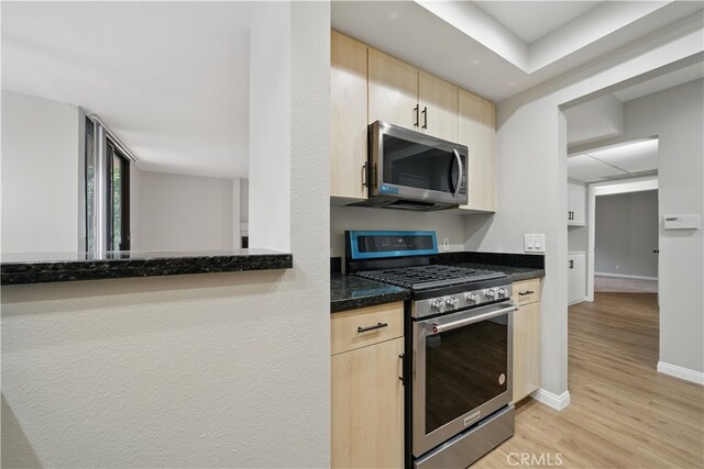7826 Topanga Canyon Blvd Unit 218, Canoga Park, CA 91304 - kitchen featuring appliances with stainless steel finishes, light brown cabinetry, light wood-style floors, baseboards, and dark stone counters