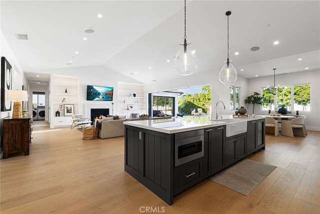 1530 Anita Ln, Newport Beach, CA 92660 - kitchen featuring stainless steel microwave, dark cabinetry, lofted ceiling, a kitchen island with sink, and light wood-style floors
