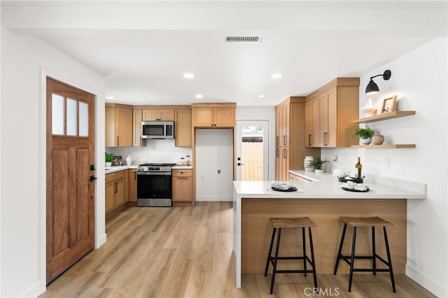 kitchen with appliances with stainless steel finishes, a peninsula, light wood-type flooring, light countertops, and recessed lighting