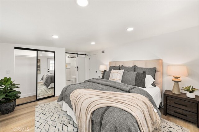 bedroom with light wood-style flooring, recessed lighting, and a barn door