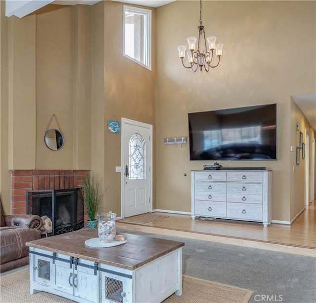 living room featuring a chandelier, healthy amount of natural light, a high ceiling, a brick fireplace, and light colored carpet