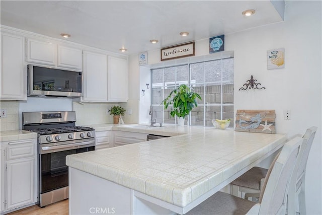 kitchen with stainless steel appliances, a peninsula, a sink, and tile countertops