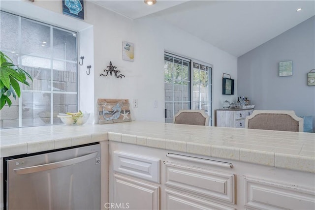 kitchen with stainless steel dishwasher, lofted ceiling, white cabinets, and tile countertops