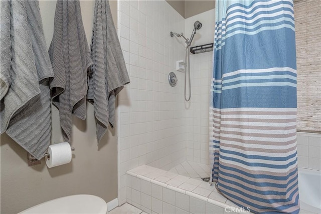 bathroom with tiled shower, toilet, and baseboards