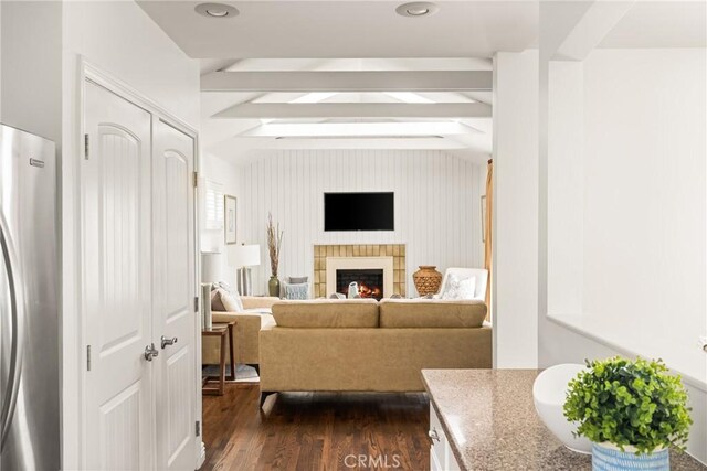 living room featuring beam ceiling, a lit fireplace, and dark wood finished floors