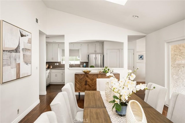 dining room with lofted ceiling, dark wood-type flooring, arched walkways, and baseboards