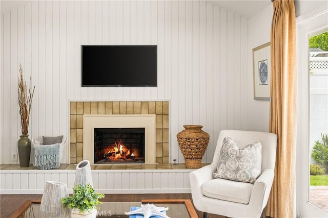 sitting room with wood finished floors, a warm lit fireplace, and wood walls