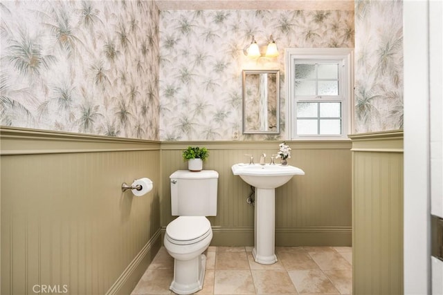 bathroom with wallpapered walls, toilet, wainscoting, tile patterned floors, and baseboards