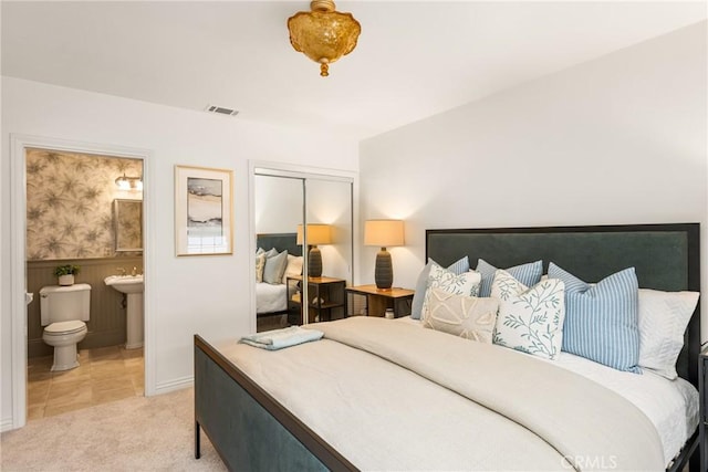 bedroom featuring a closet, a wainscoted wall, light carpet, and connected bathroom