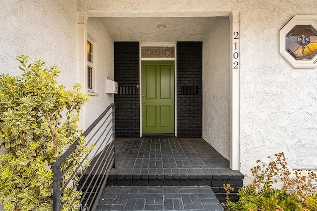 property entrance featuring stucco siding, brick siding, and a porch