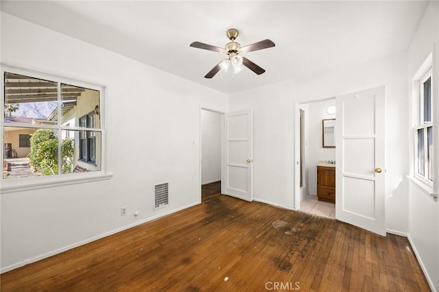 unfurnished bedroom with hardwood / wood-style flooring, baseboards, connected bathroom, and a ceiling fan