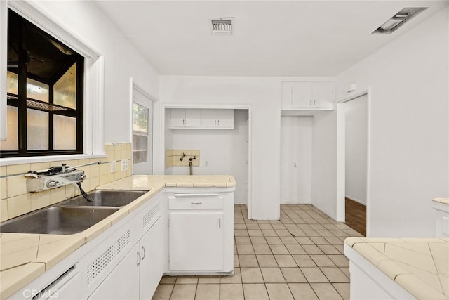 kitchen with a sink, tile counters, white cabinetry, decorative backsplash, and a peninsula
