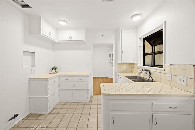 kitchen featuring a peninsula, a sink, tasteful backsplash, light tile patterned flooring, and white cabinets