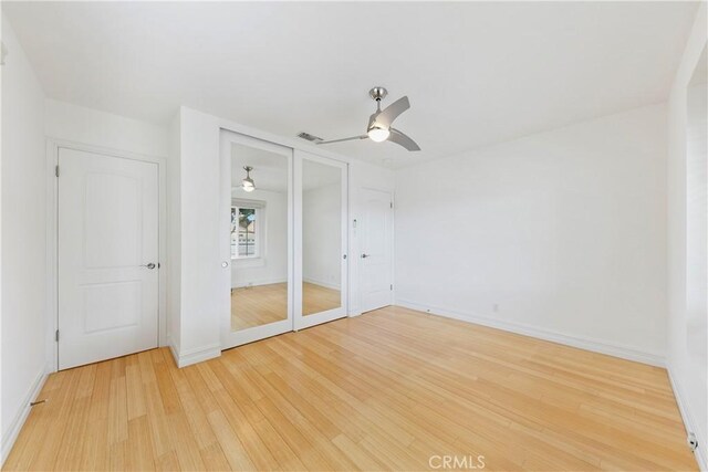 unfurnished bedroom with light wood finished floors, baseboards, two closets, and a ceiling fan