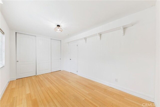 unfurnished bedroom featuring light wood-style flooring, baseboards, and a closet
