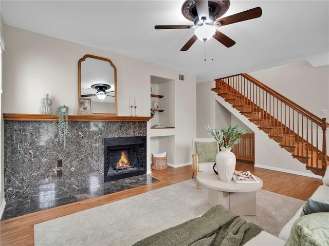 living room featuring ceiling fan, stairway, a tiled fireplace, wood finished floors, and baseboards