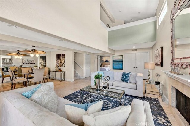 living area featuring stairs, a premium fireplace, a ceiling fan, baseboards, and a high ceiling