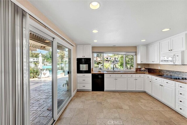 kitchen featuring black appliances, a sink, stone tile floors, white cabinets, and recessed lighting