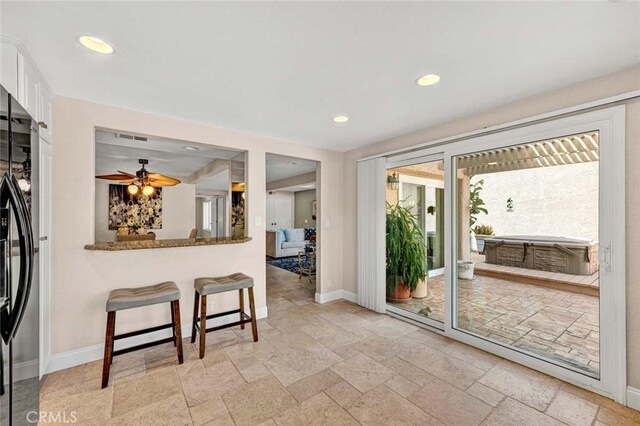 interior space featuring baseboards, stone tile flooring, black refrigerator with ice dispenser, ceiling fan, and recessed lighting
