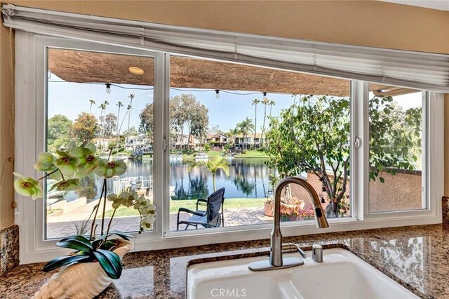 kitchen view of a sink, a water view, stone counters, and a residential view