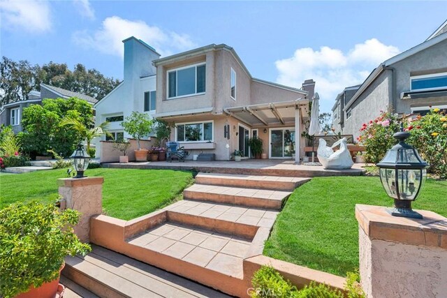 rear view of property featuring a patio, a yard, and stucco siding