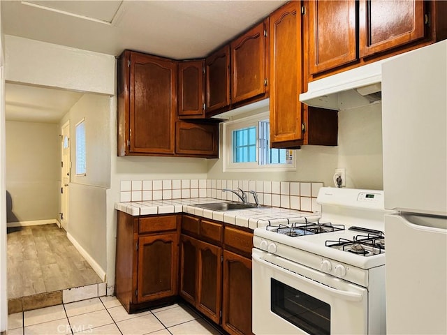 kitchen with white appliances, a sink, light tile patterned floors, tile countertops, and baseboards