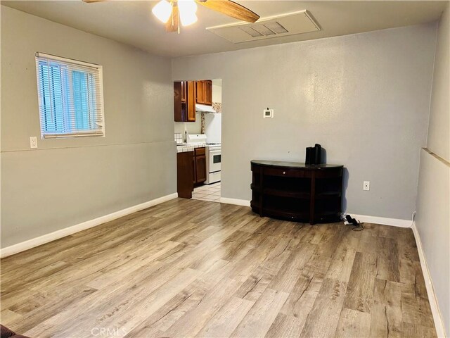 unfurnished room featuring ceiling fan, light wood finished floors, attic access, and baseboards