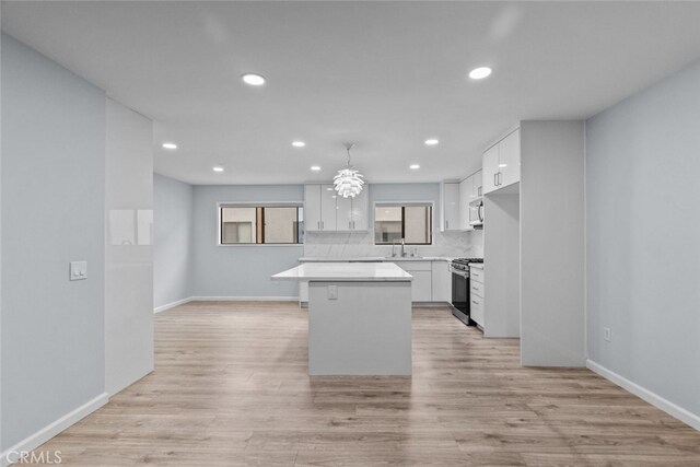 kitchen featuring stainless steel range with gas cooktop, a kitchen island, white cabinetry, light countertops, and baseboards