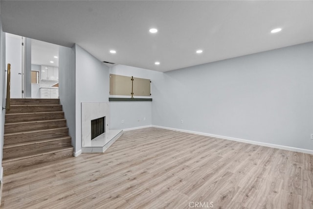 unfurnished living room with light wood finished floors, recessed lighting, baseboards, stairs, and a premium fireplace