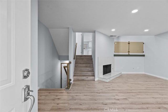 basement featuring light wood finished floors, recessed lighting, a high end fireplace, baseboards, and stairway
