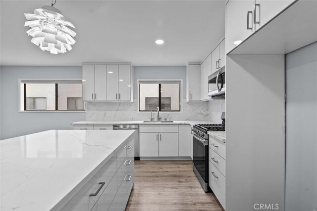 kitchen featuring stainless steel appliances, a sink, backsplash, light wood-style flooring, and recessed lighting