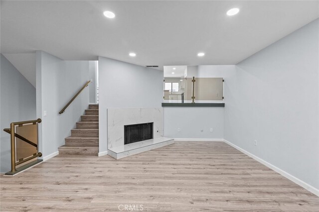 unfurnished living room featuring wood finished floors, stairs, recessed lighting, a premium fireplace, and baseboards
