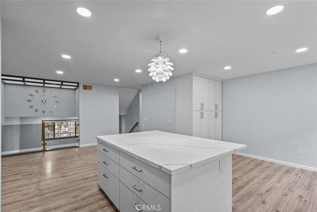 kitchen featuring recessed lighting, light wood-style flooring, a center island, decorative light fixtures, and light stone counters