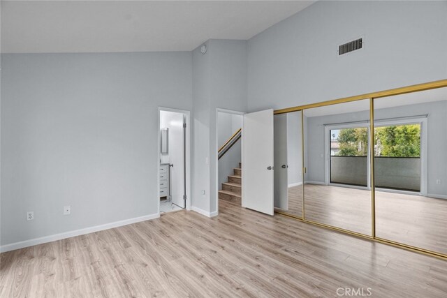unfurnished bedroom featuring high vaulted ceiling, wood finished floors, baseboards, ensuite bath, and access to outside
