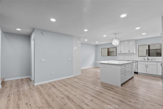 kitchen featuring a center island, white cabinets, light countertops, a sink, and light wood finished floors