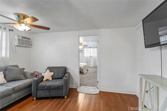 living area featuring ceiling fan, a wall mounted air conditioner, wood finished floors, and baseboards