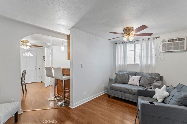 living room featuring a ceiling fan, wood finished floors, a textured ceiling, a wall unit AC, and arched walkways