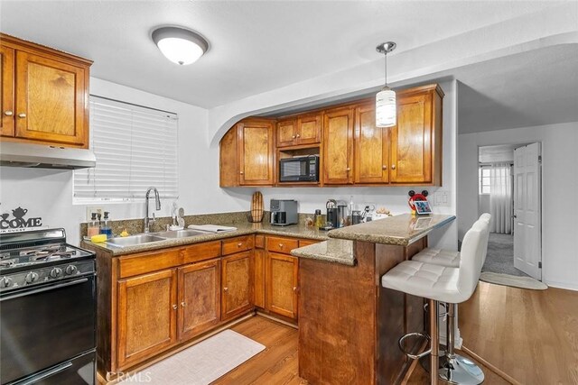 kitchen featuring black appliances, under cabinet range hood, a sink, light wood-type flooring, and a kitchen breakfast bar
