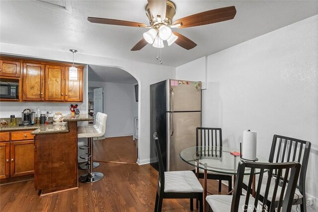 dining area featuring arched walkways, dark wood finished floors, a ceiling fan, and baseboards