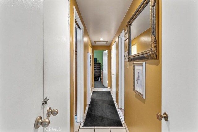 corridor featuring tile patterned floors, baseboards, and attic access