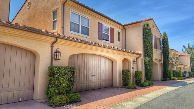 view of front of house with a garage, stucco siding, a tile roof, and decorative driveway