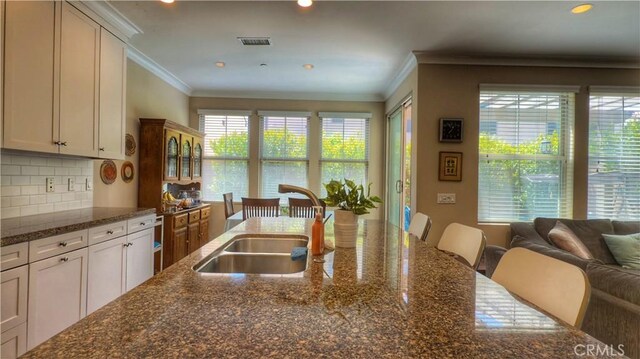 kitchen featuring crown molding, a sink, backsplash, dark stone counters, and a kitchen breakfast bar