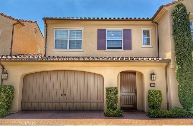 mediterranean / spanish-style house with stucco siding, driveway, an attached garage, and a tile roof