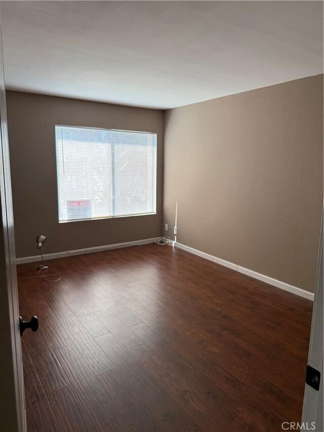 empty room with dark wood-type flooring and baseboards