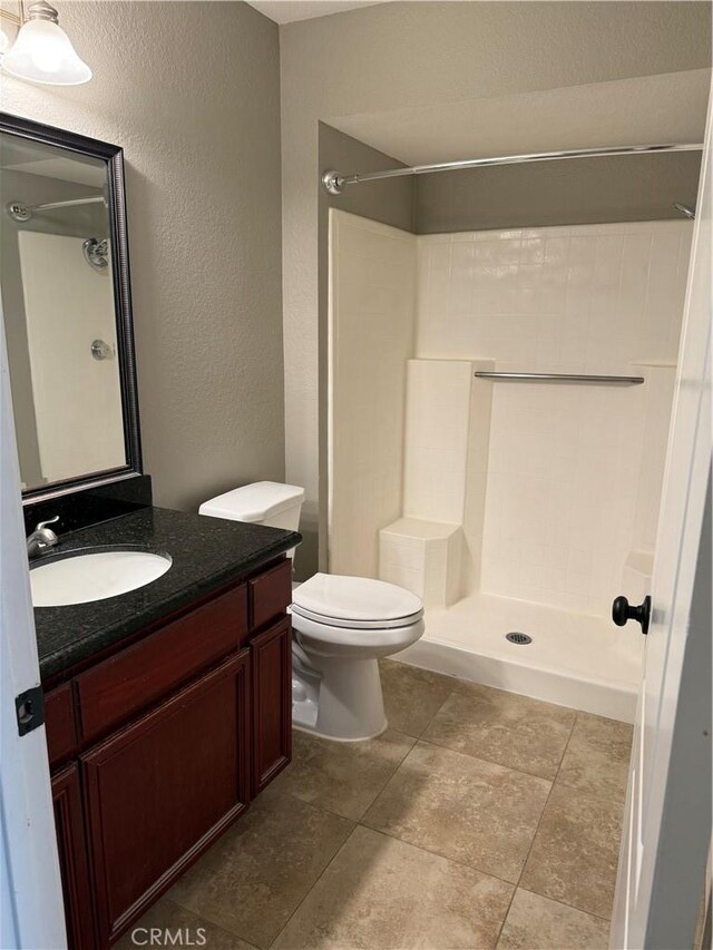 full bath with a textured wall, vanity, toilet, and tiled shower
