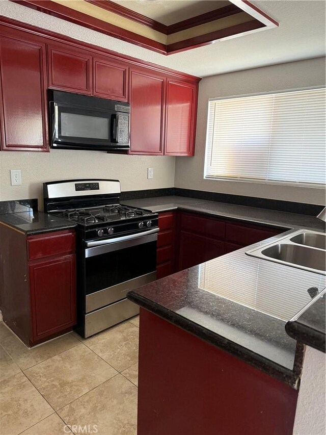 kitchen with black microwave, stainless steel gas range, dark brown cabinets, dark countertops, and a sink